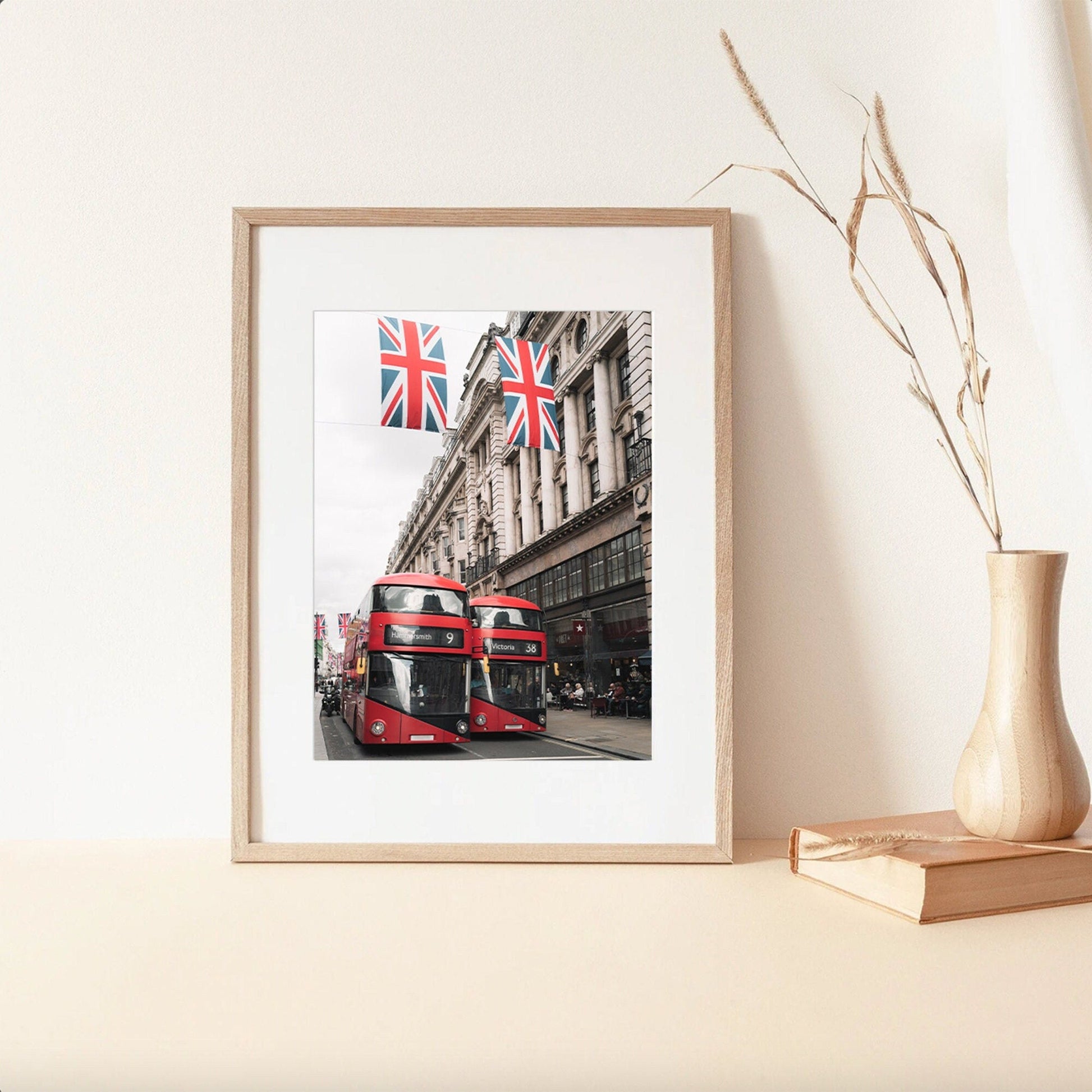 Double-deckers photo with Union Jack flags leaning on beige wall, next to a wooden vase and books.