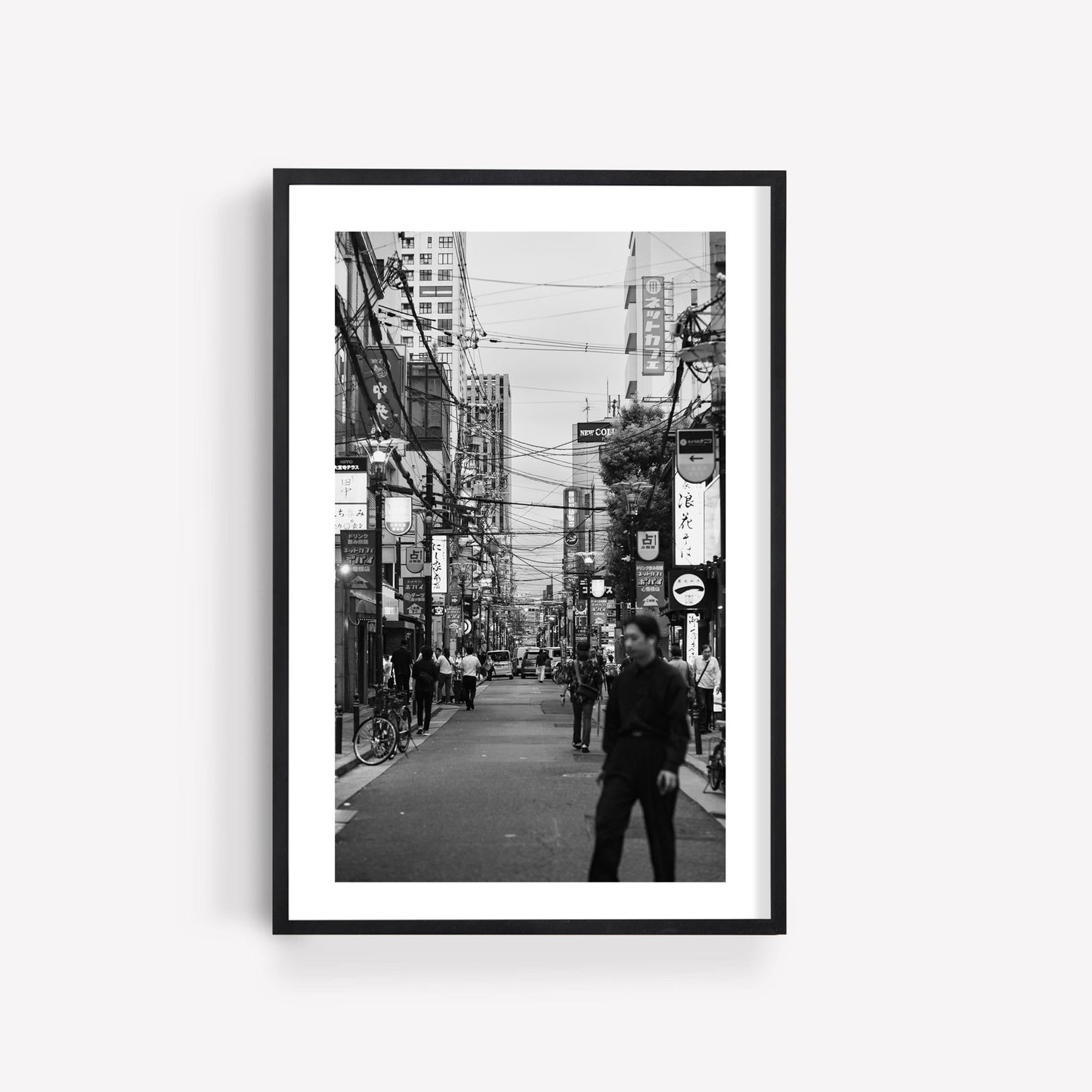 Echoes of Osaka Black and White: framed city street photo with people and buildings, displayed on a white wall.