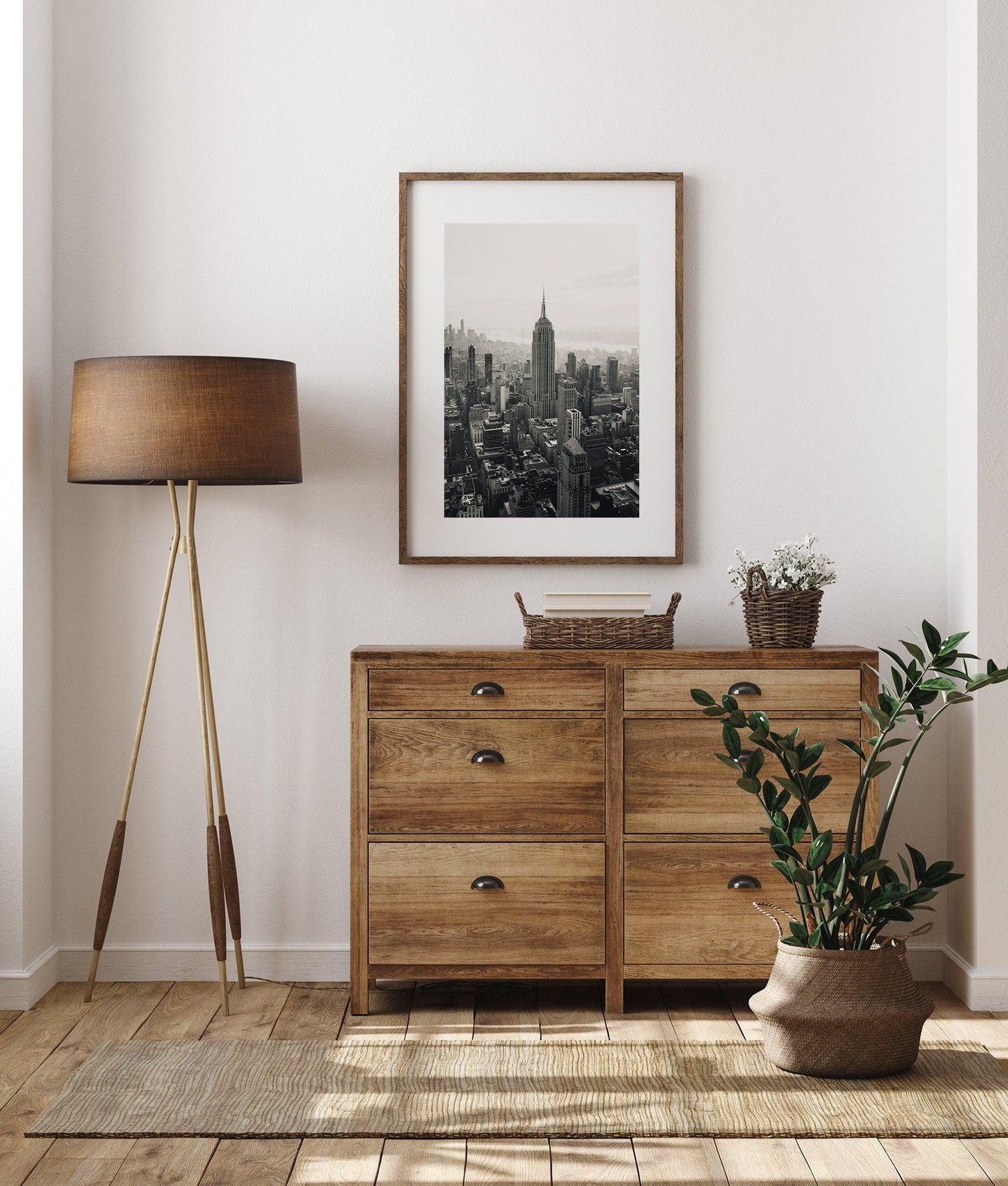 Minimalist room with a wooden dresser, floor lamp, potted plant, and Empire State Building photo on the wall.