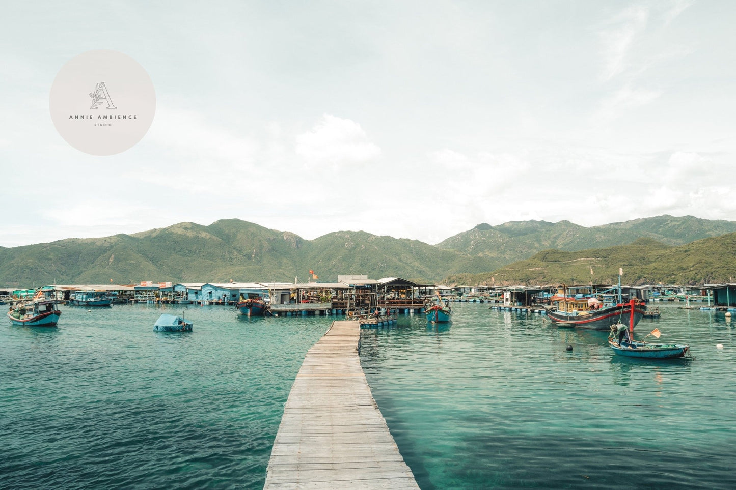 Wooden pier leading to Fishing Village I on a calm, greenish-blue sea with mountains in the background.