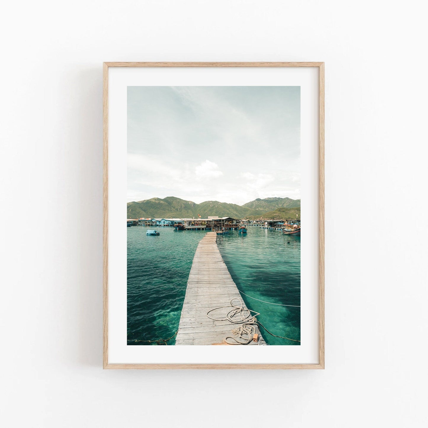 Framed photo Fishing Village II shows a wooden pier stretching over calm waters towards mountains and a clear sky.