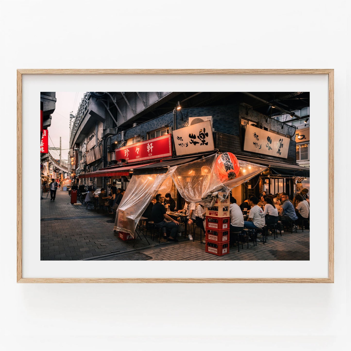 Framed photo "Flavors Of Ueno" shows people dining outdoors at a lively Japanese street restaurant under clear coverings.