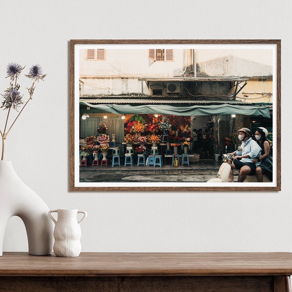 Floral Ride: A framed photo of a flower shop, featuring two people on a scooter, displayed on a minimalist wall.