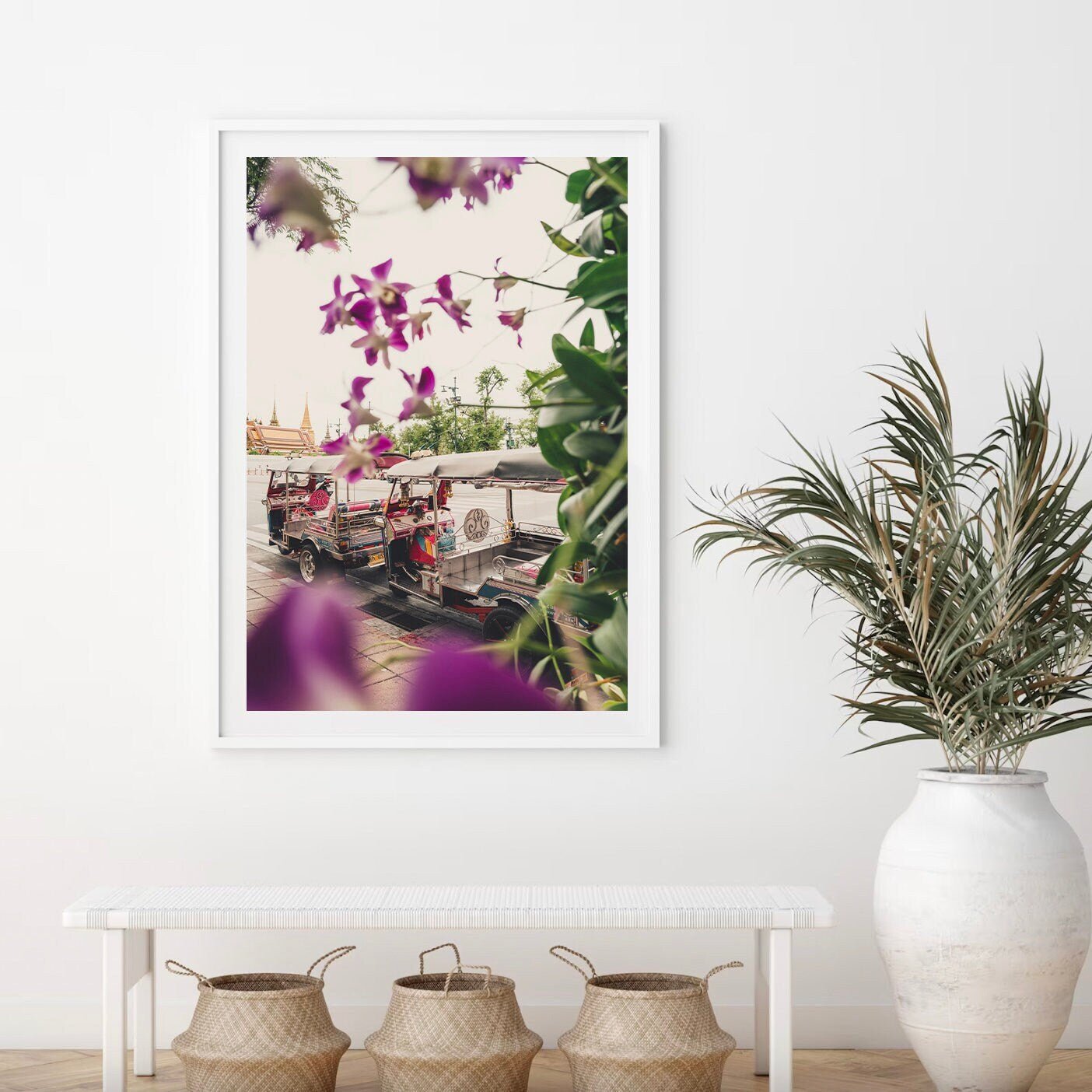The Floral Tuktuk photo hangs above a bench with woven baskets, showcasing tuk-tuks in a cityscape and purple flowers.