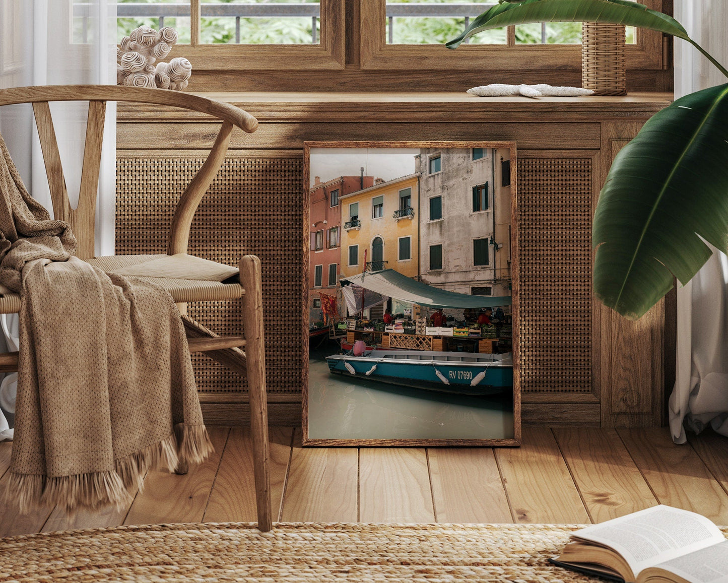 A framed Fruit Boat photo leans against a wooden cabinet in a cozy room with a chair and an open book.