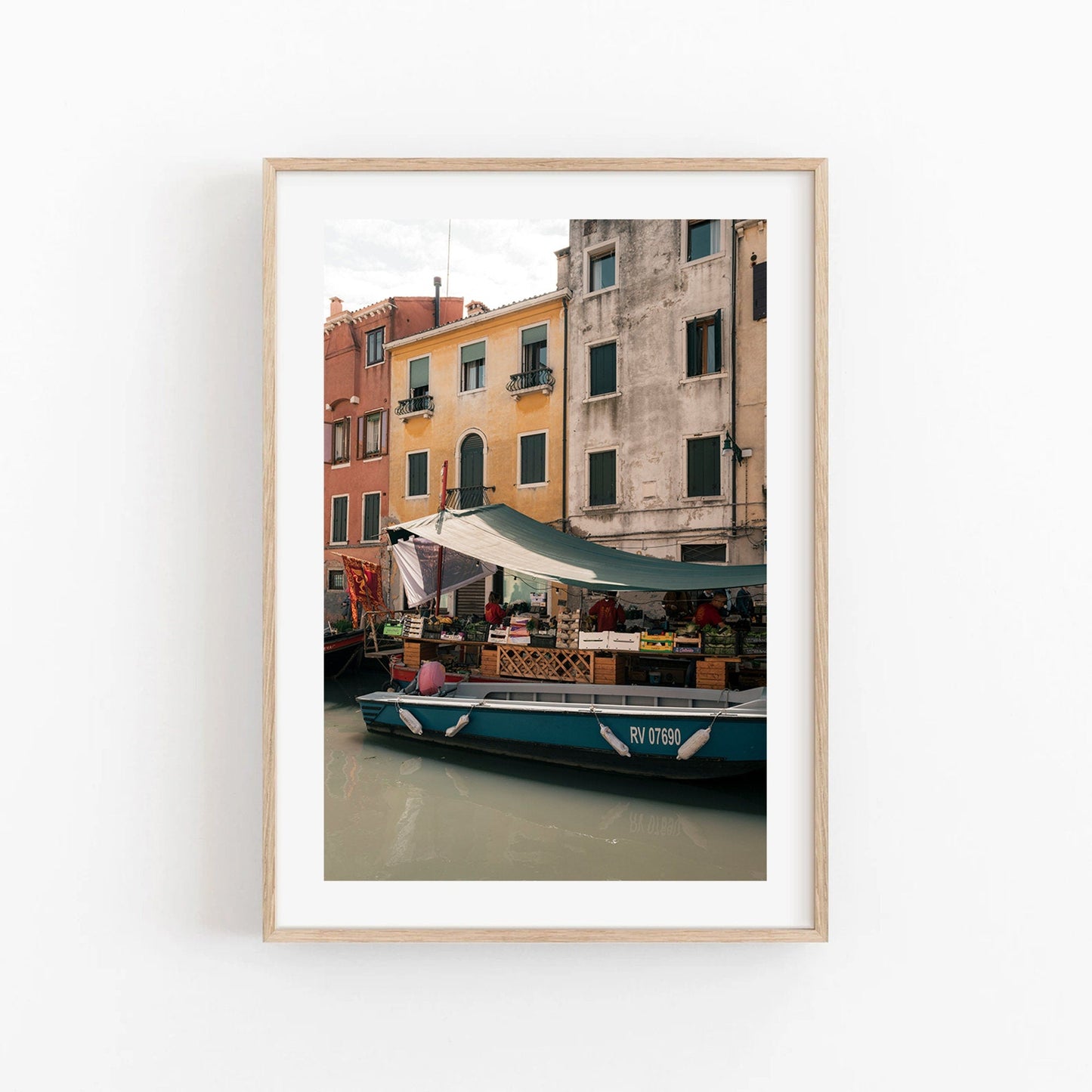 Framed photo titled Fruit Boat shows a canal with colorful buildings and a blue boat carrying goods under a tarp.