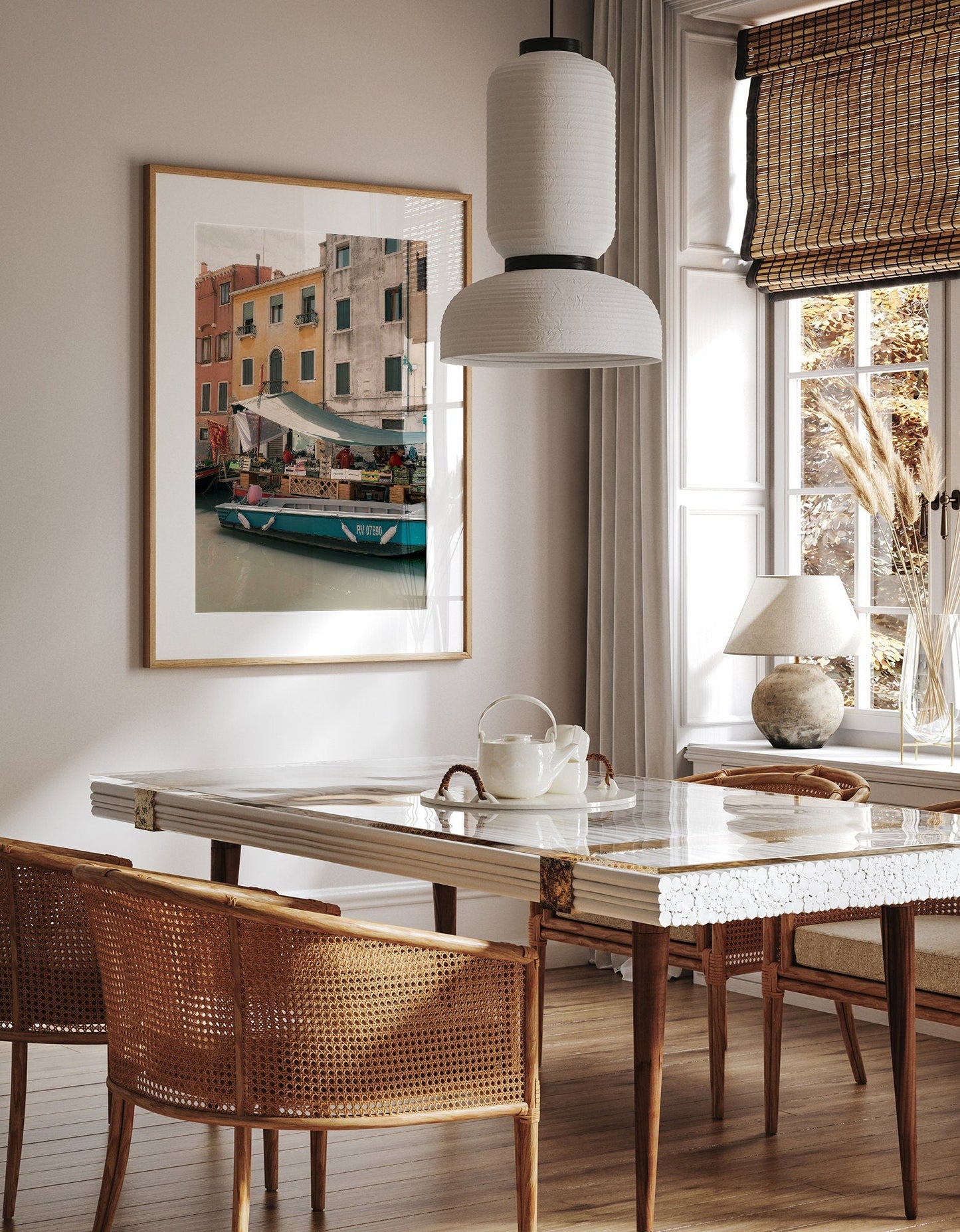 A cozy dining area featuring wicker chairs, a marble table, pendant lamp, and the Fruit Boat artwork on the wall.