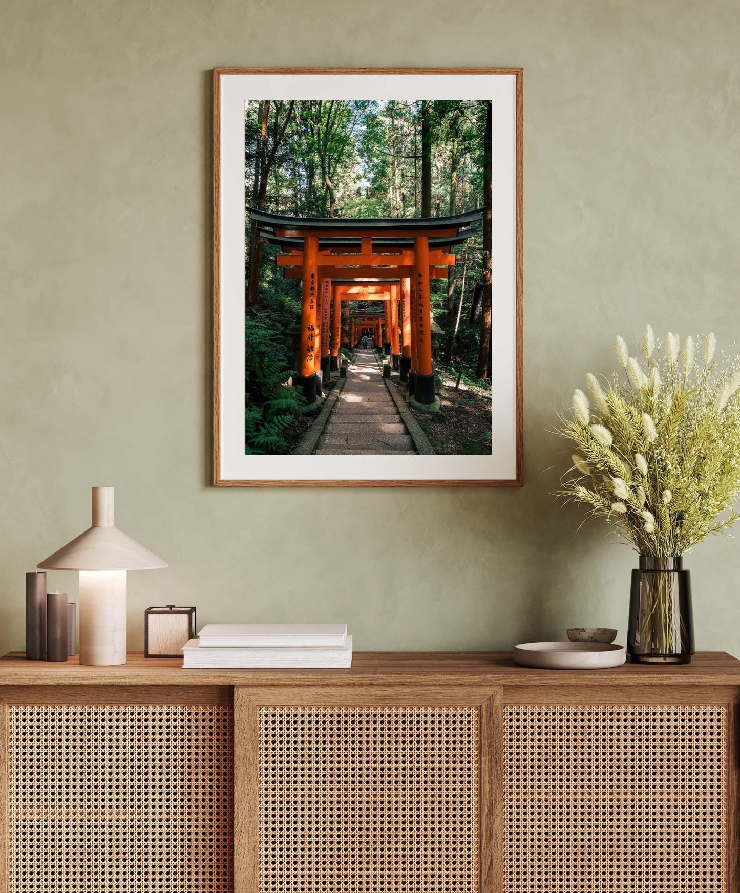 Framed Fushimi Inari Taisha I photo on a wall above a wooden cabinet adorned with a lamp, books, and a flower vase.
