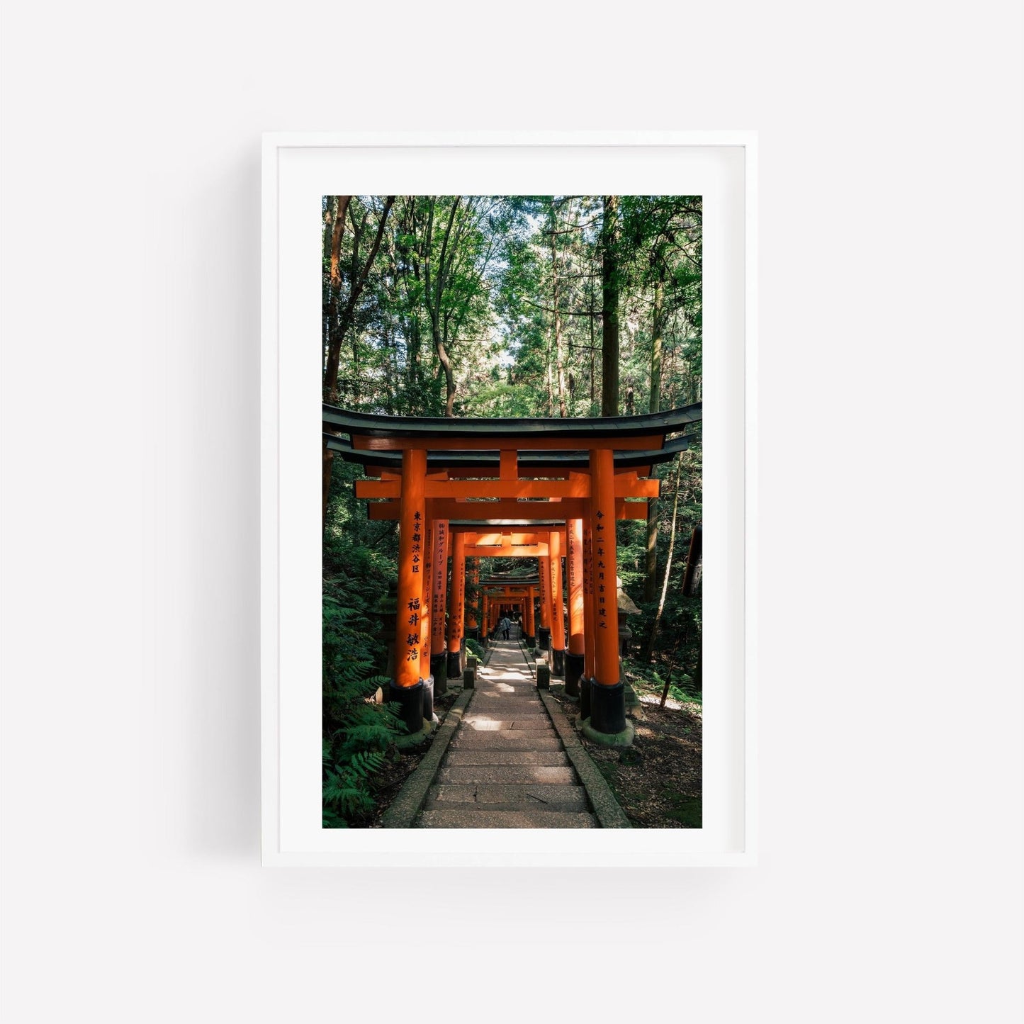 Framed photo titled Fushimi Inari Taisha I depicting an orange torii gate path through a forest with lush greenery.