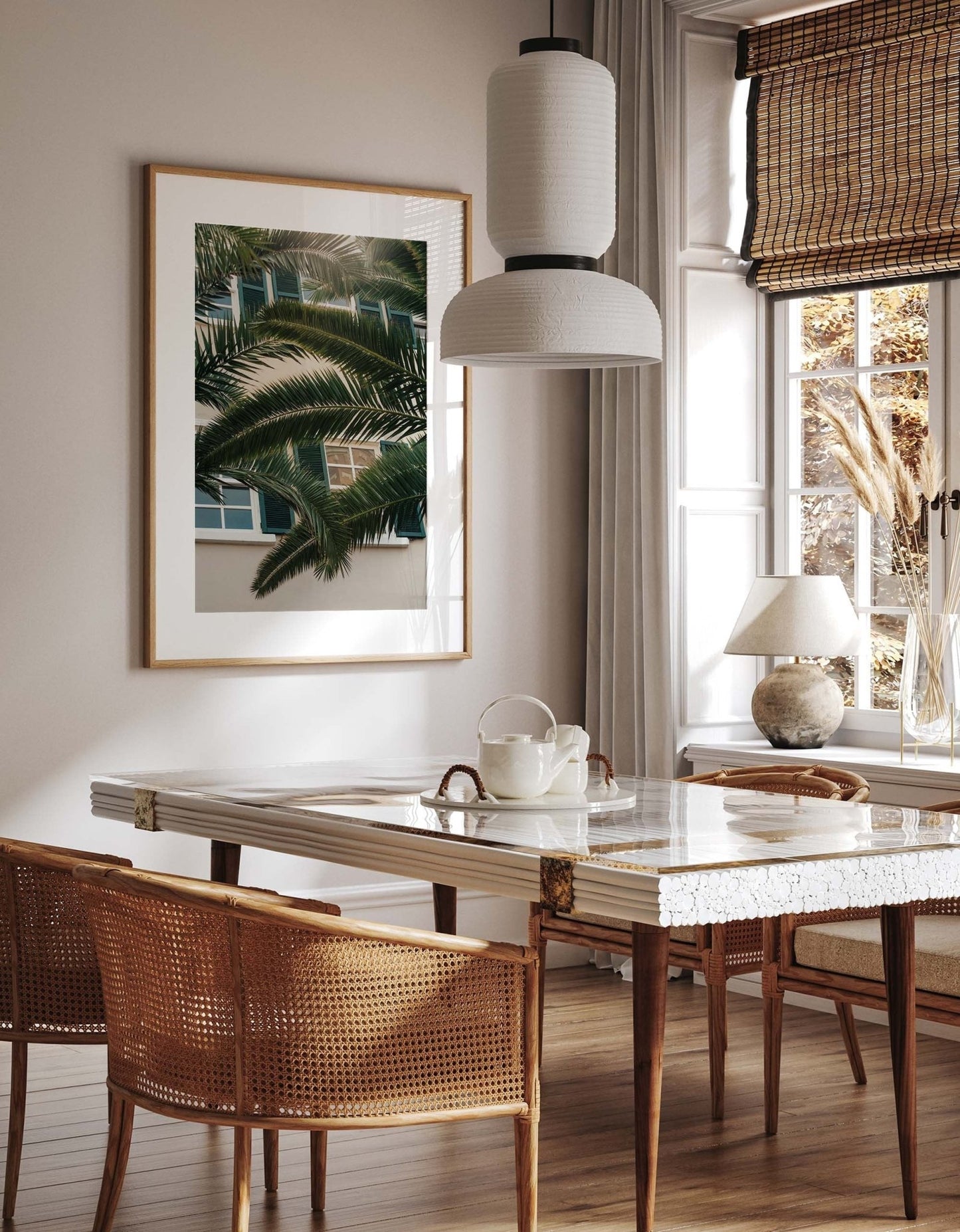 A stylish dining room with a marble table, wicker chairs, and a large Gibraltar Palm print under a pendant light.
