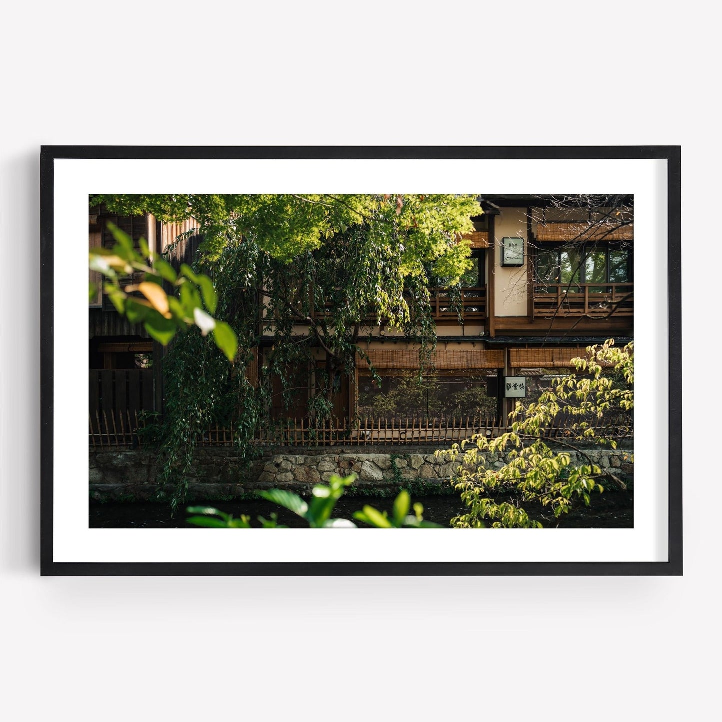 Gion Greenery: A framed photograph capturing a traditional Japanese building amid lush greenery and a serene canal.