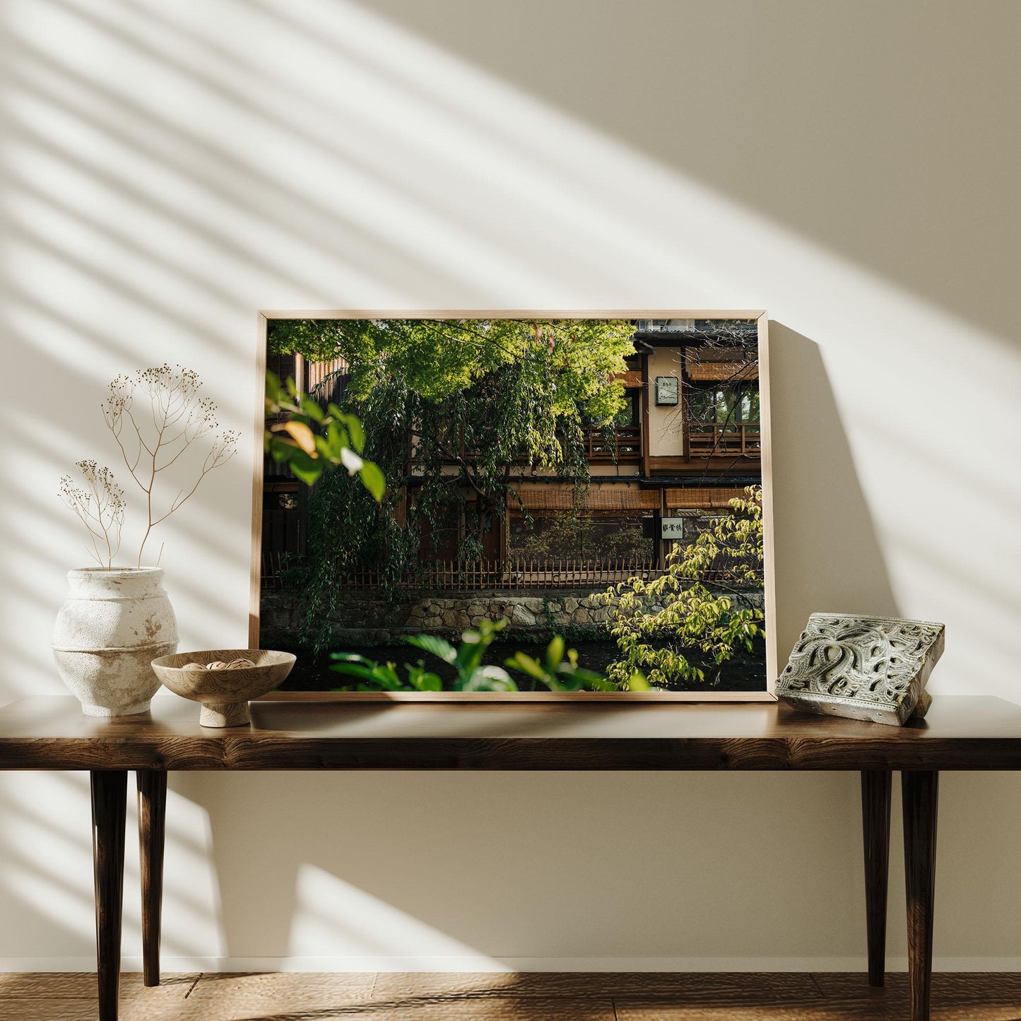 The Gion Greenery nature photo is framed and displayed on a table with decor, touched by sunlight and shadows against the wall.