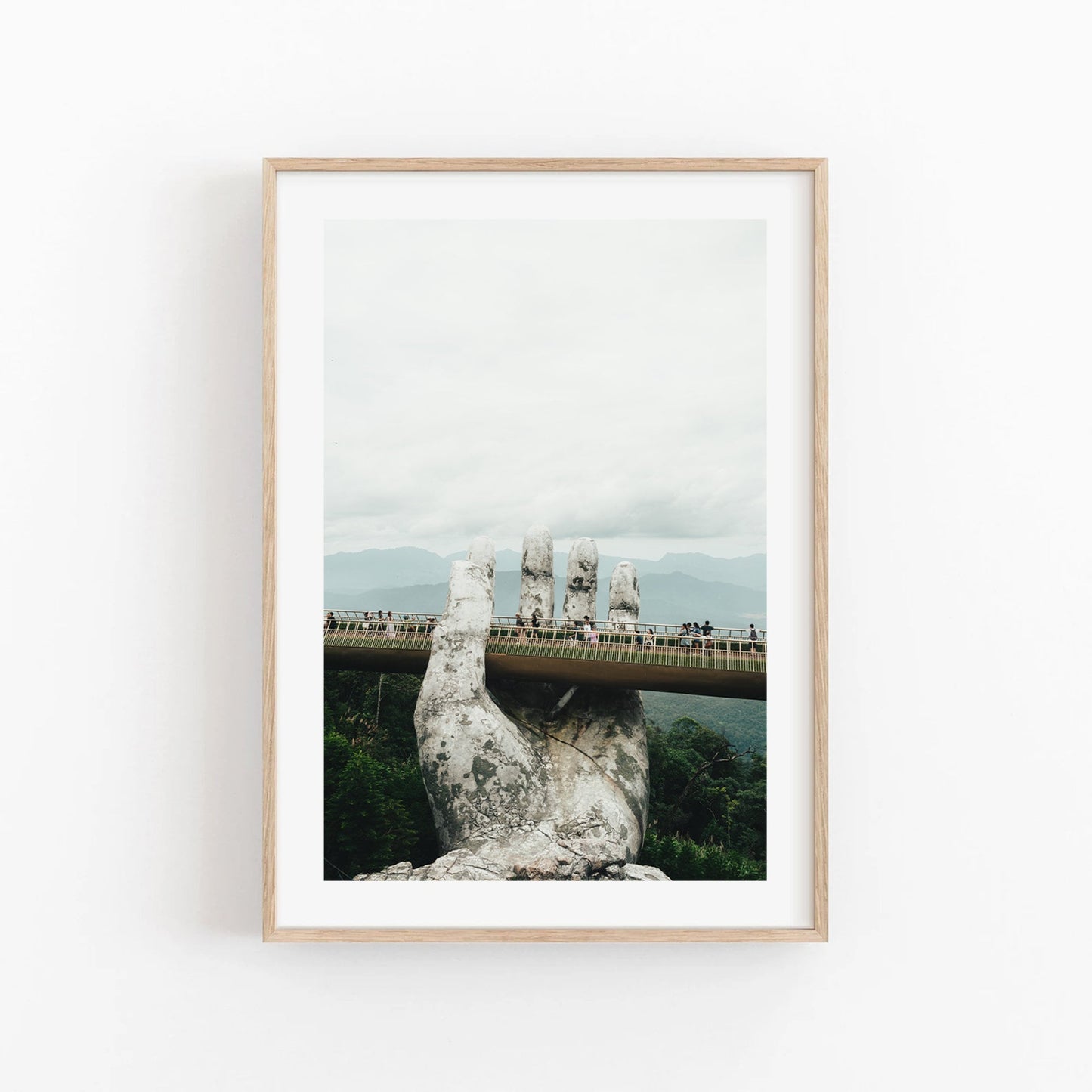 Framed photo titled Golden Hand Bridge I depicts a stone hand holding a pedestrian bridge with tourists against clouds and mountains.