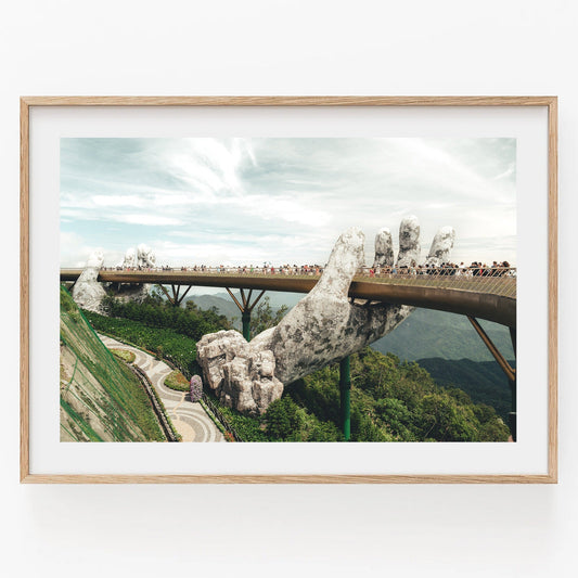 A framed photo of the Golden Hand Bridge II in Vietnam, with hands supporting the walkway amid lush greenery.