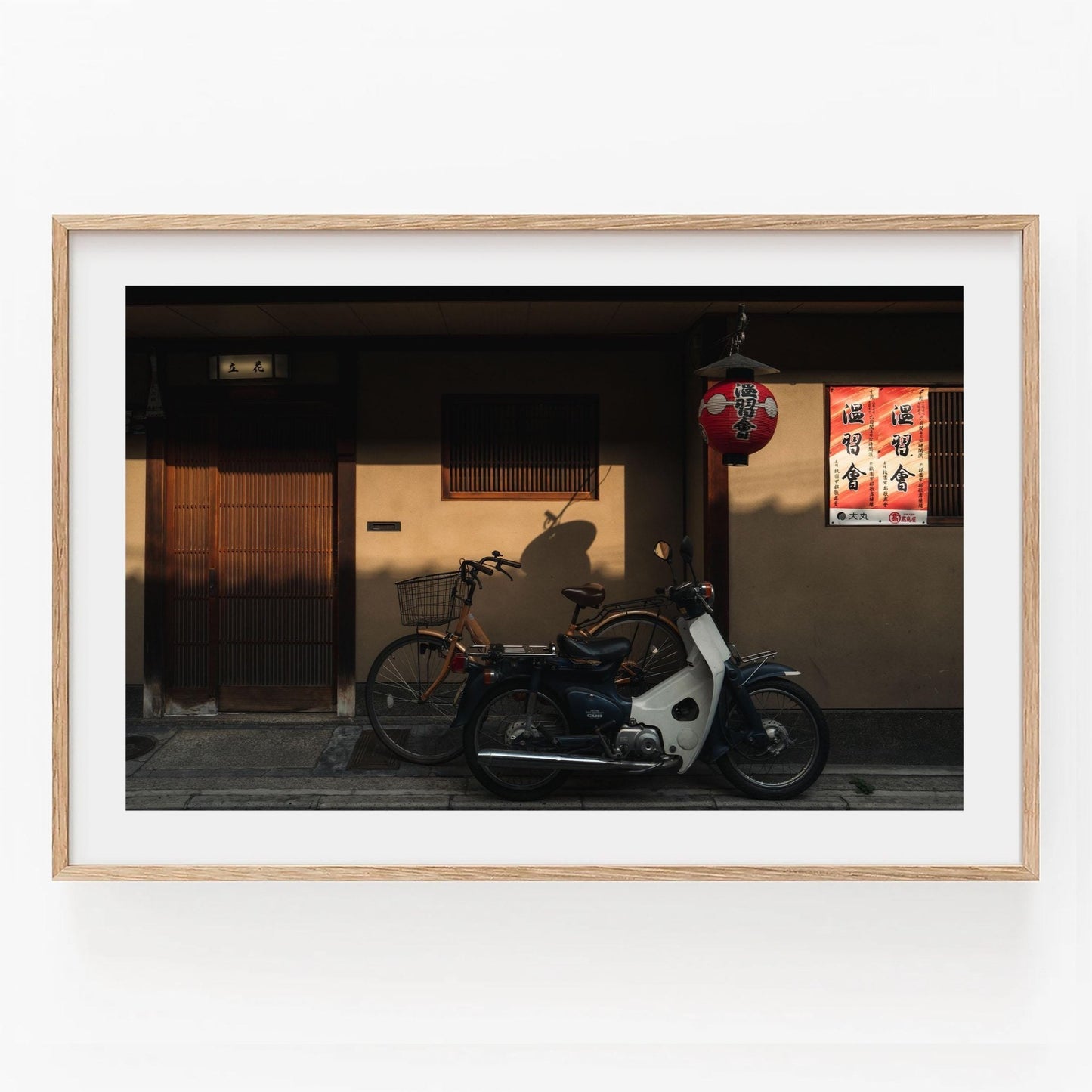 Framed photo titled Golden Shadow, featuring a bicycle and moped parked outside a building with a lantern and posters on the wall.