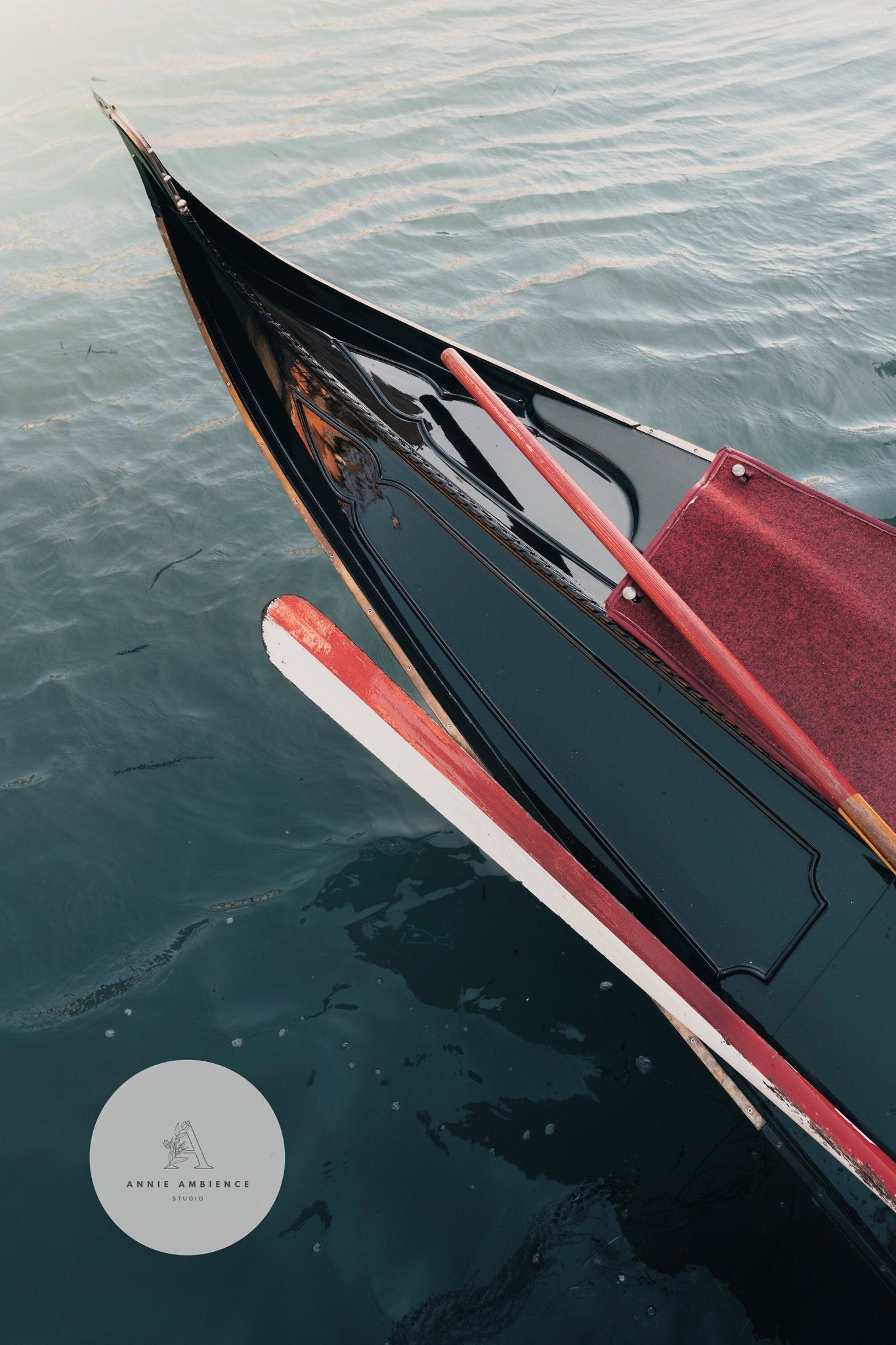 Close-up of a Gondolas bow on calm water, featuring a red velvet seat and wooden oar.