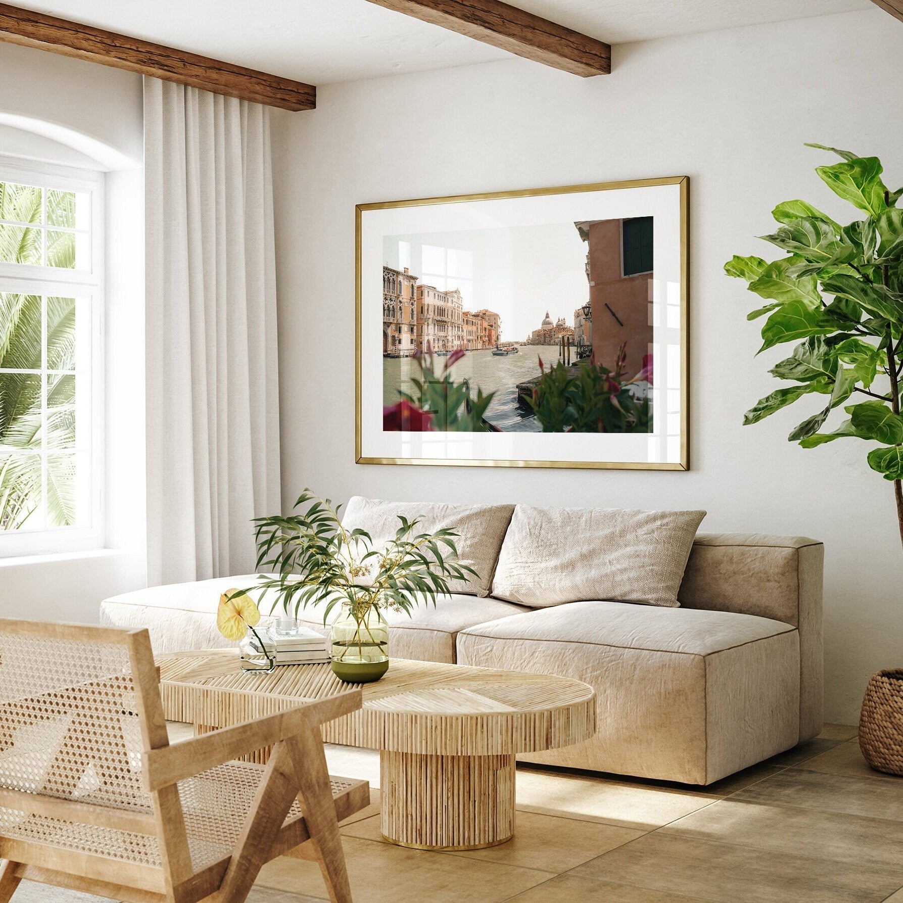 Bright living room with a beige sofa, wooden furniture, plants, and a framed painting titled Grand Canal on the wall.