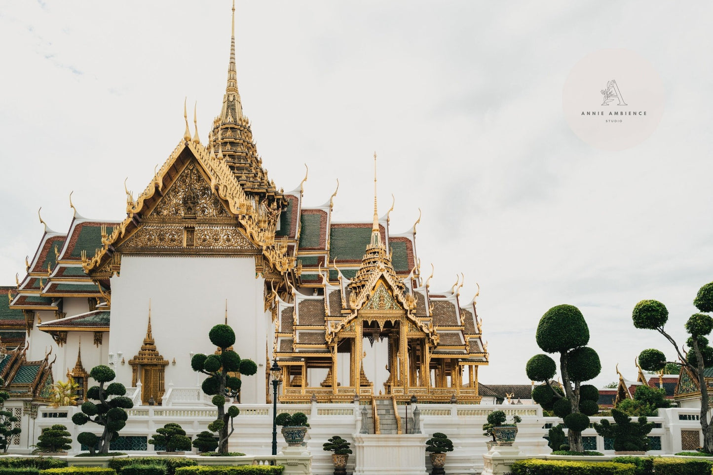 An ornate Grand Palace VII with golden spires, surrounded by manicured trees and a cloudy sky.