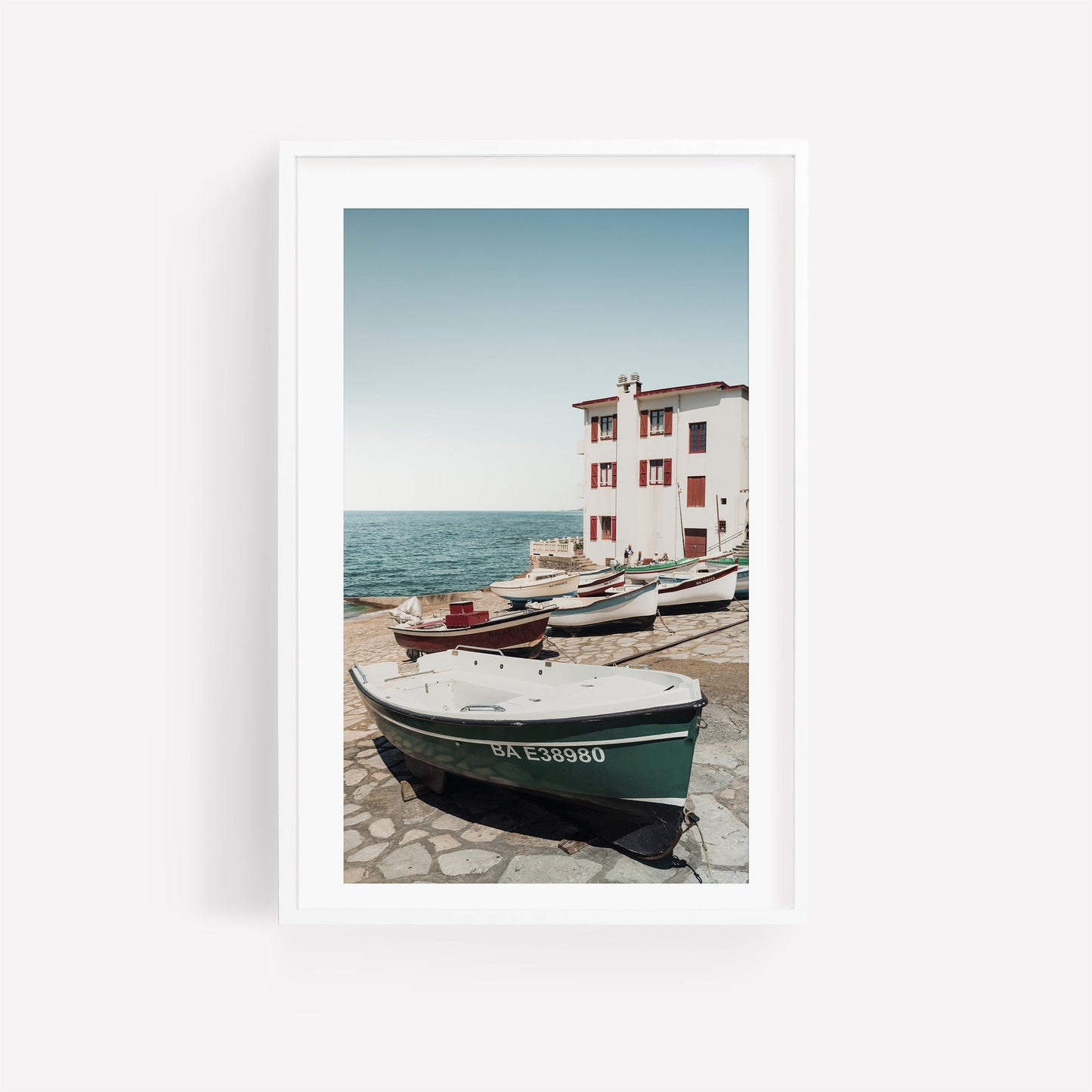 Framed photo Guethary: boats on a stone dock by the sea, with a white building and clear blue sky.