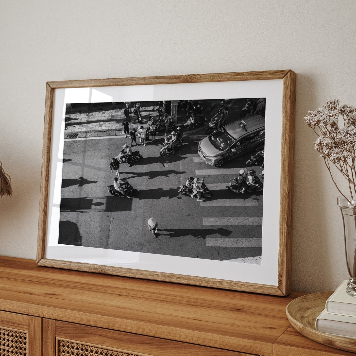 Hanoi Street Crossing Black & White framed photo of scooters and a car on a street, displayed on a wooden sideboard.