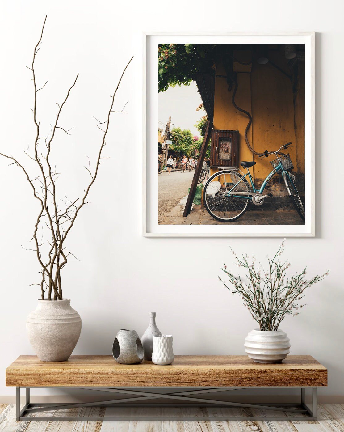 A minimalist room with the Hoi An Bike photo, vases, and bare branches on a wooden console table.