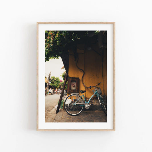 Framed Hoi An Bike photo: a blue bicycle against a yellow wall on a street.