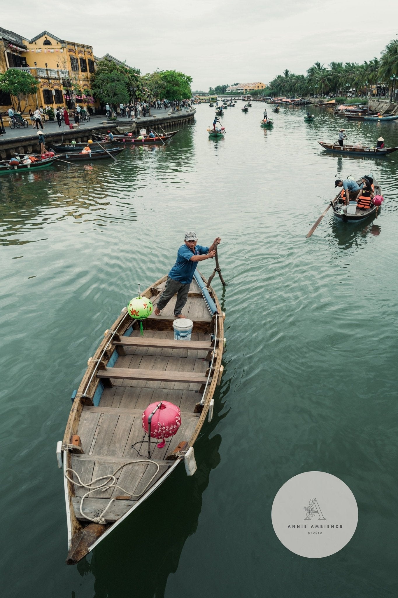 A man rows his boat in Hoi An Row amidst colorful ornaments with other boats and people nearby.