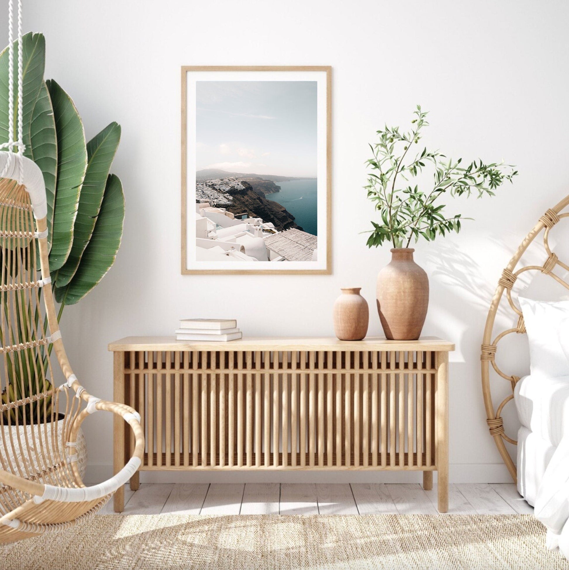 Minimalist room featuring the Imerovigli painting, a wicker chair, potted plants, and decor in neutral tones.