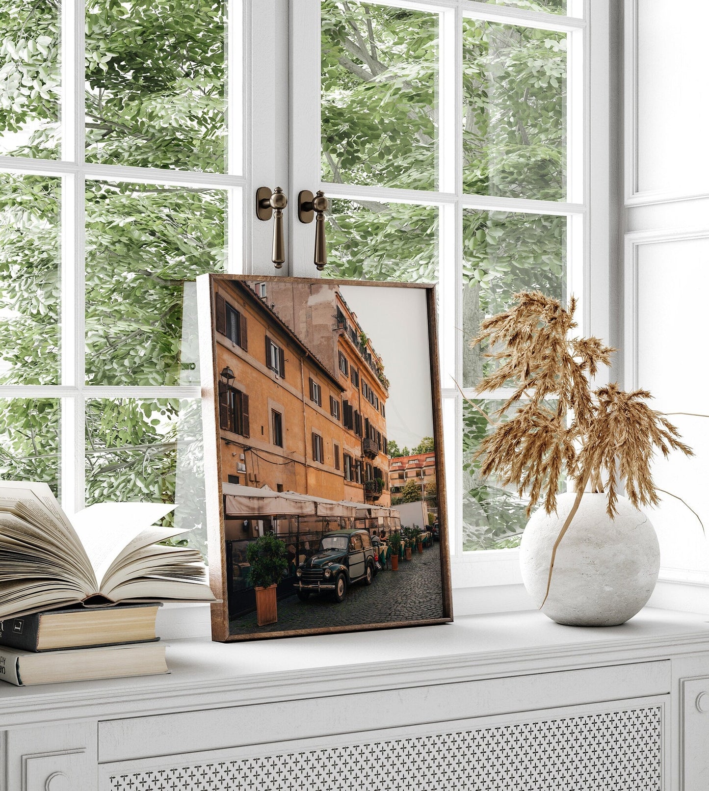 An Italian Car photo in a frame leans on a windowsill beside an open book and dried flowers.