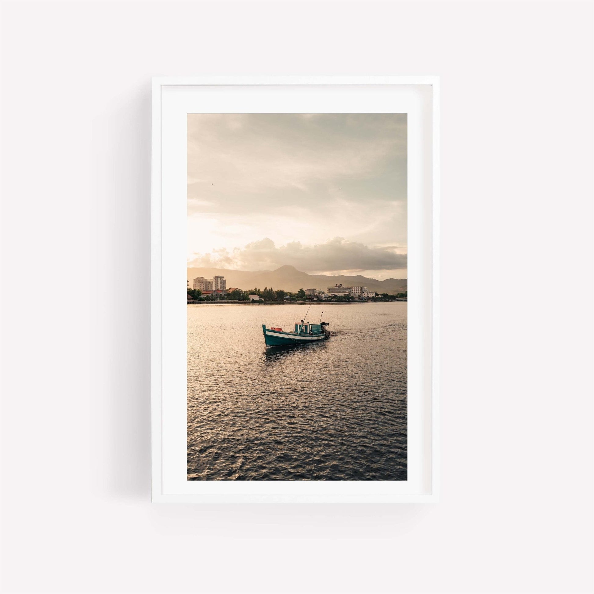 The Kampot Boat on calm waters with a city skyline and mountains in the sunset background.