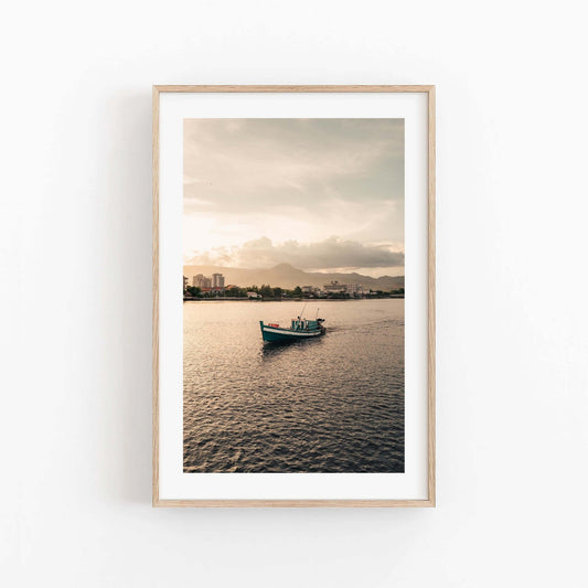 Framed Kampot Boat photo: boat on calm water at sunset, distant city skyline, cloudy sky.