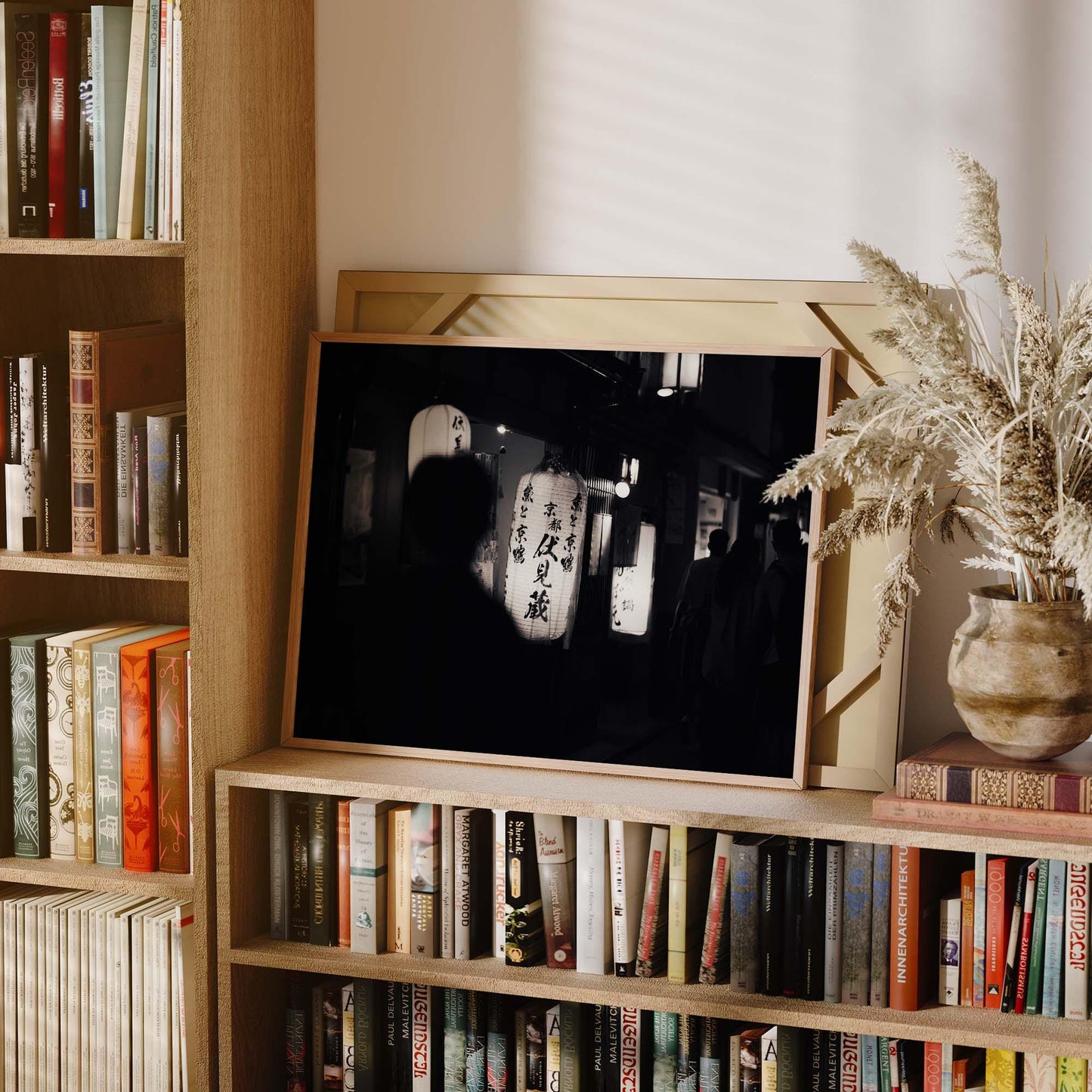 The Kyoto At Night Black and White framed photo with Japanese lanterns sits on a bookshelf with books and dried grasses.