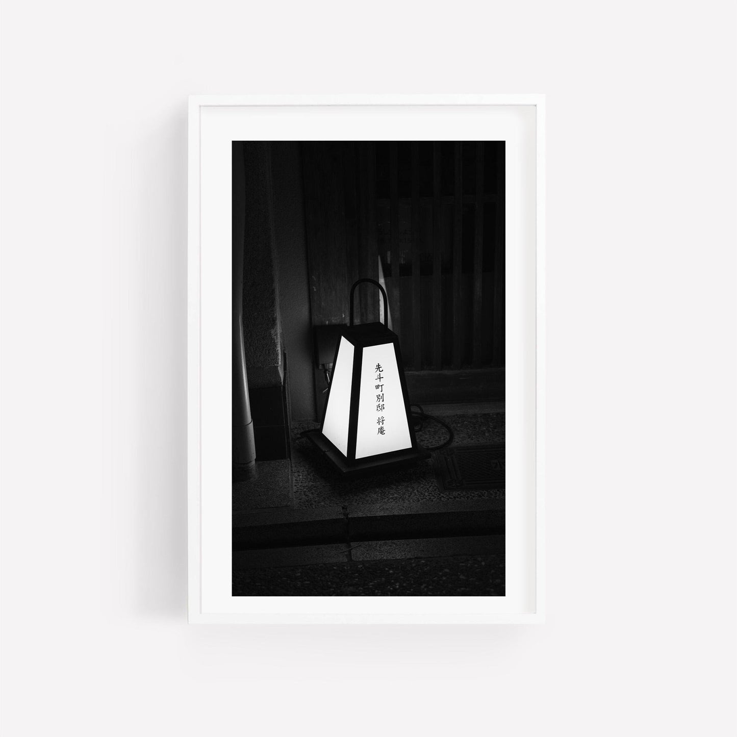 Black and white photo of Kyoto Lantern placed on the ground before a wooden door, featuring Japanese text.