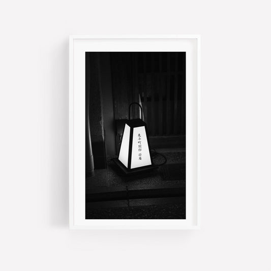 Black and white photo of Kyoto Lantern placed on the ground before a wooden door, featuring Japanese text.