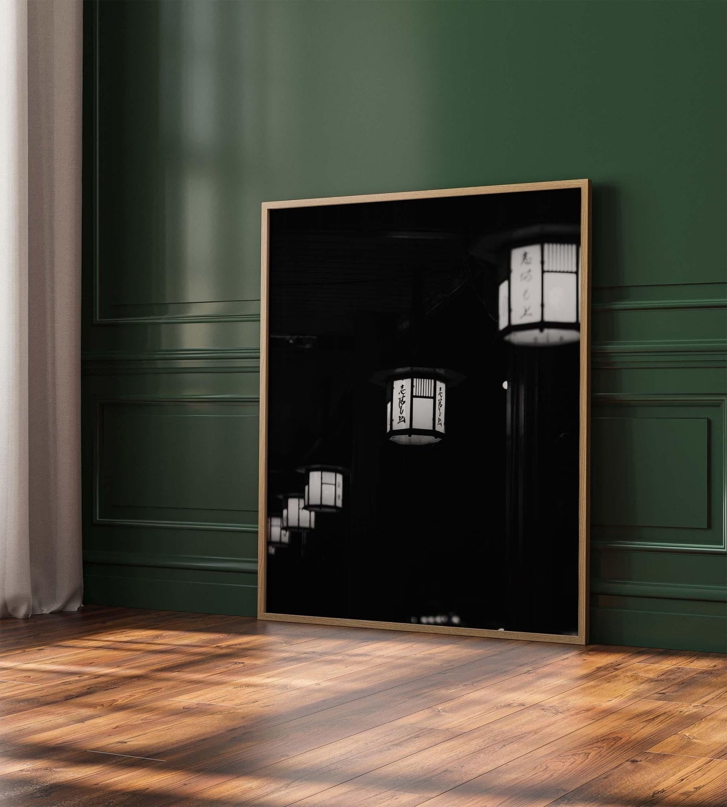 The Kyoto Lanterns II Black and White framed photo leans against a dark green wall on a sunlit wooden floor.