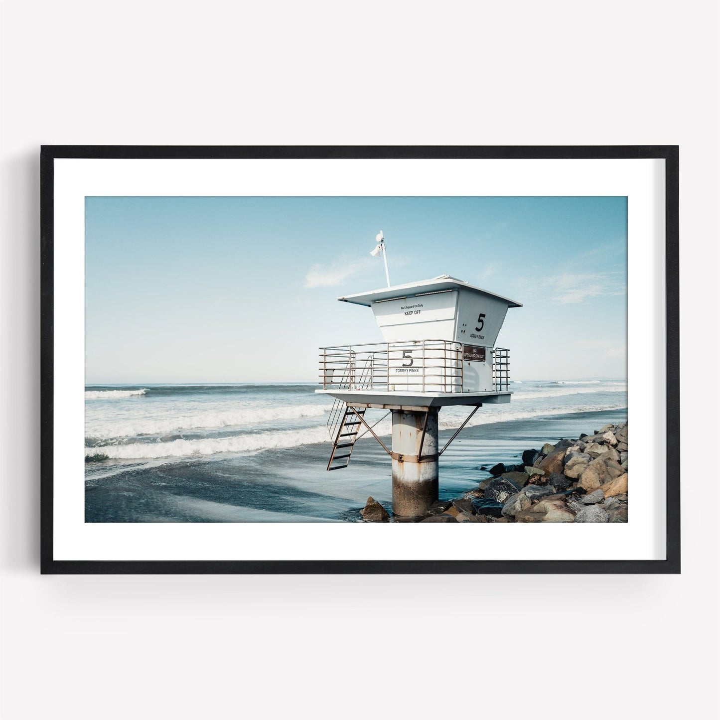 Framed photo: Lifeguard Tower on a rocky beach under a clear blue sky.