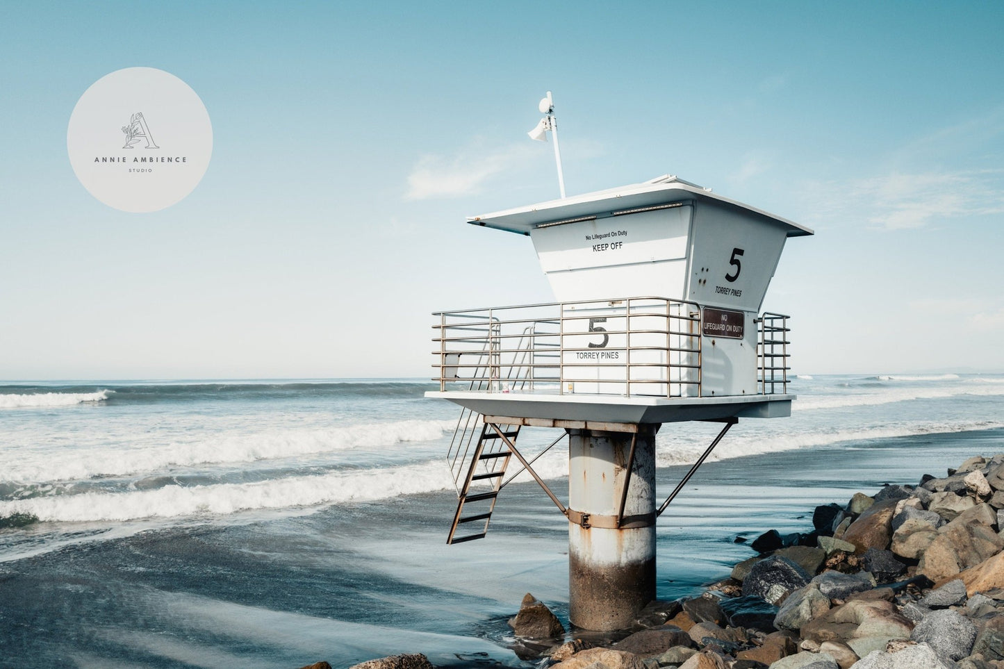 Lifeguard Tower on a rocky beach with waves and a blue sky background.