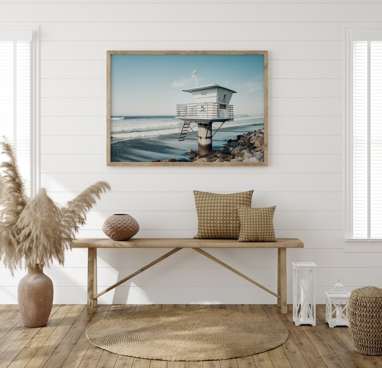 Coastal-themed room with a Lifeguard Tower photo, wooden bench, cushions, and dried plants.