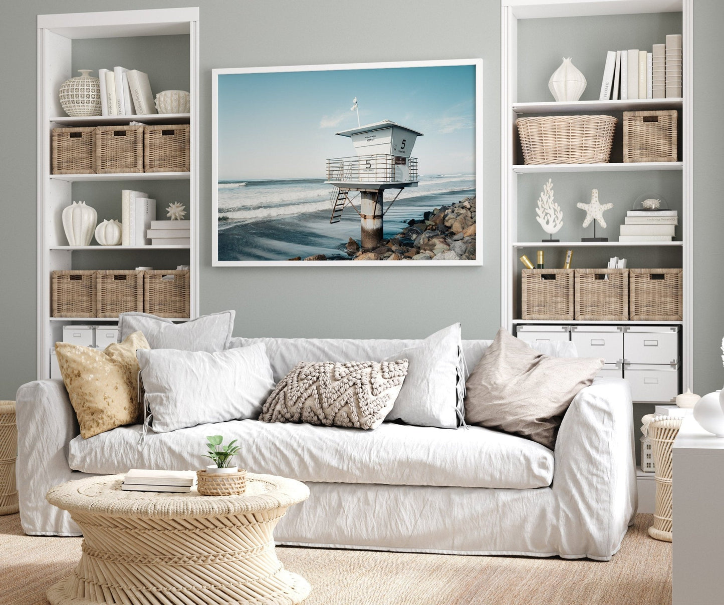 Beach-themed living room with a white sofa, wicker baskets, and Lifeguard Tower ocean photo on the wall.