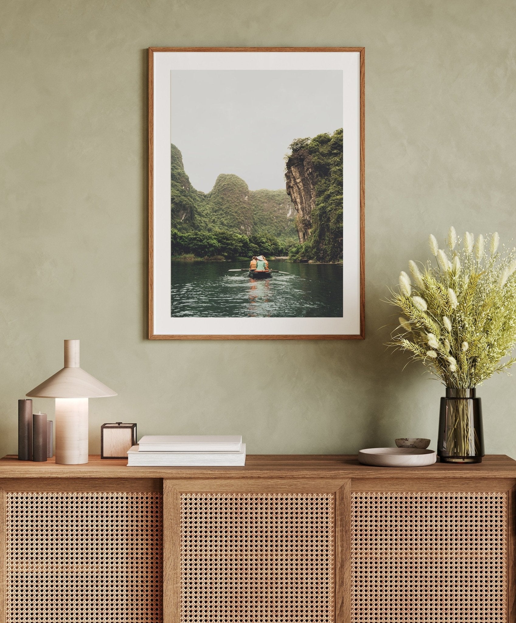 Framed Limestone Waterway photo on a wall above a wooden sideboard with a lamp, books, and a vase of flowers.