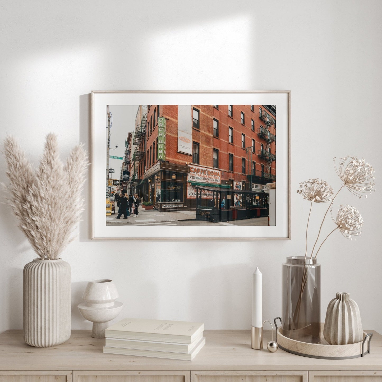 The Little Italy II cityscape photo adorns a wall above a beige console with vases, dried plants, and stacked books.