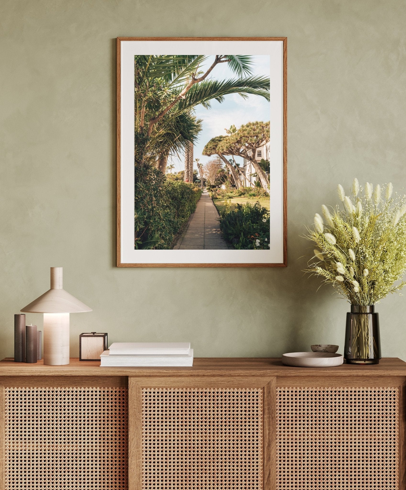 The Loma Lane picture hangs above a wooden cabinet with books, a lamp, and flowers.