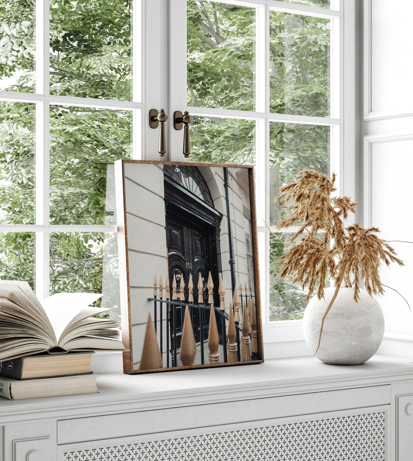 The London Door framed photo sits on a windowsill near an open book and a vase with dried plants.