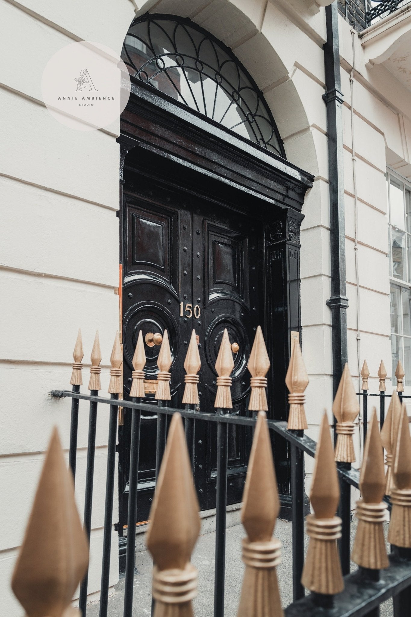 London Door: Ornate black with number 150, decorative transom window, and spiked metal fence.