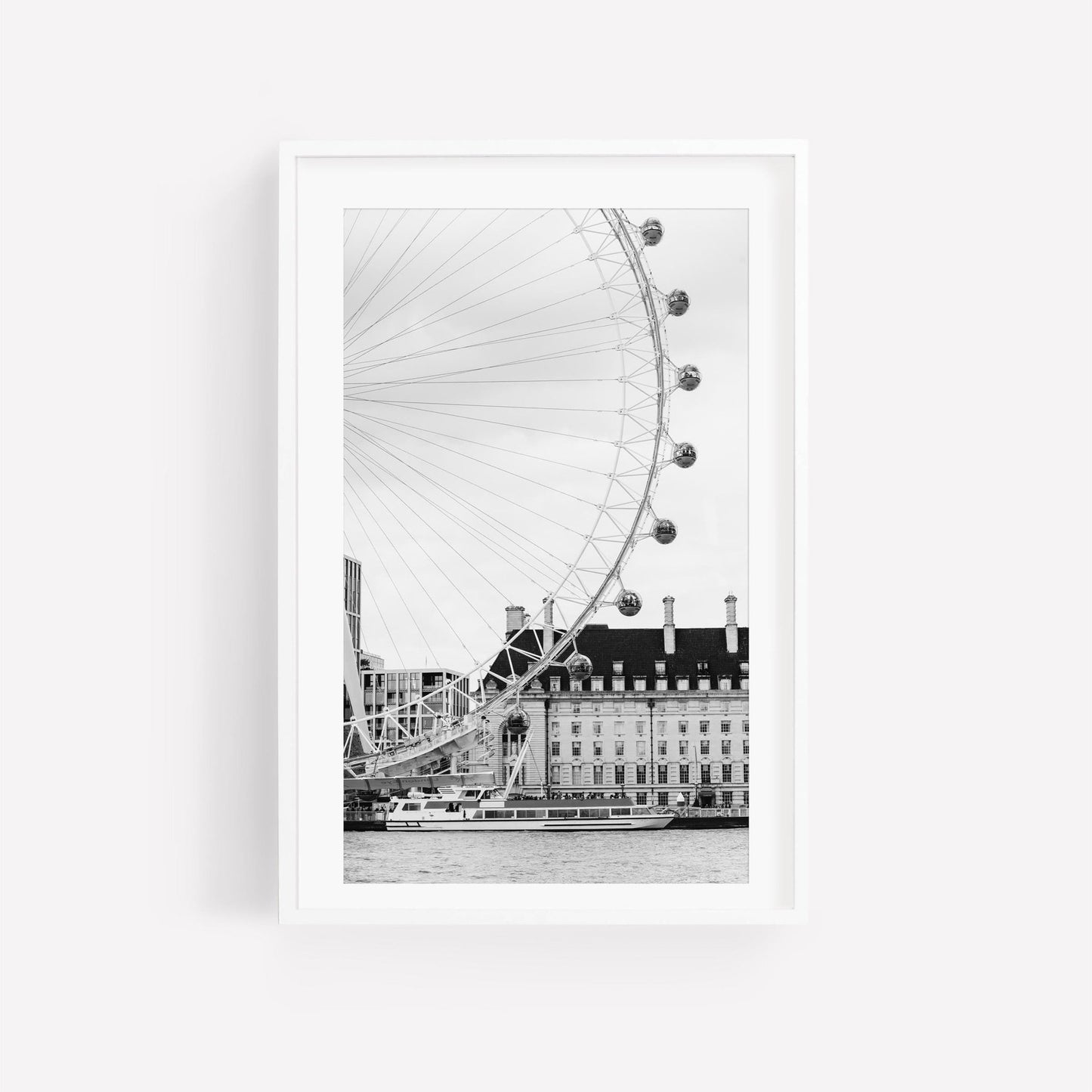 Black and white photo of the London Eye by a riverside building with a passing boat.