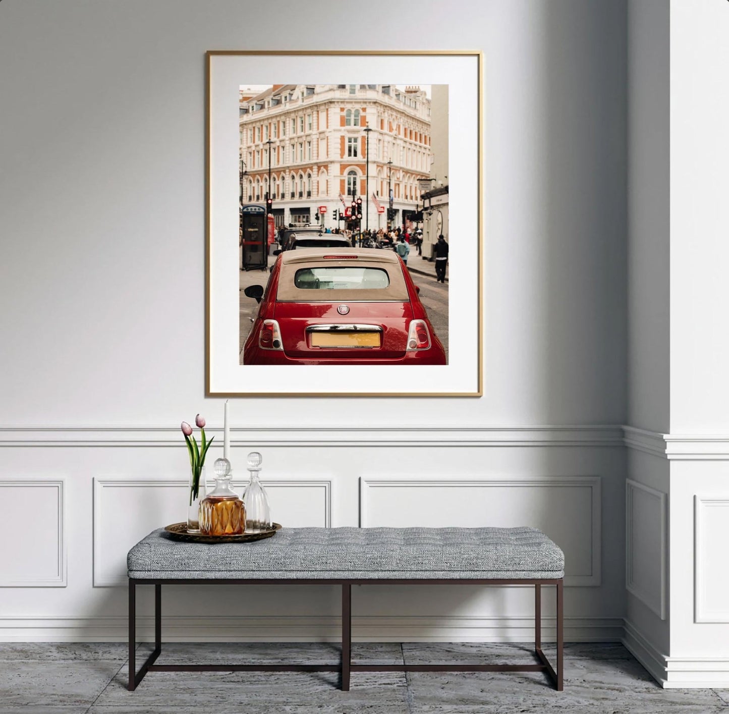 A framed London Fiat photo above a bench with flowers and a decanter in a stylish, minimalist room.