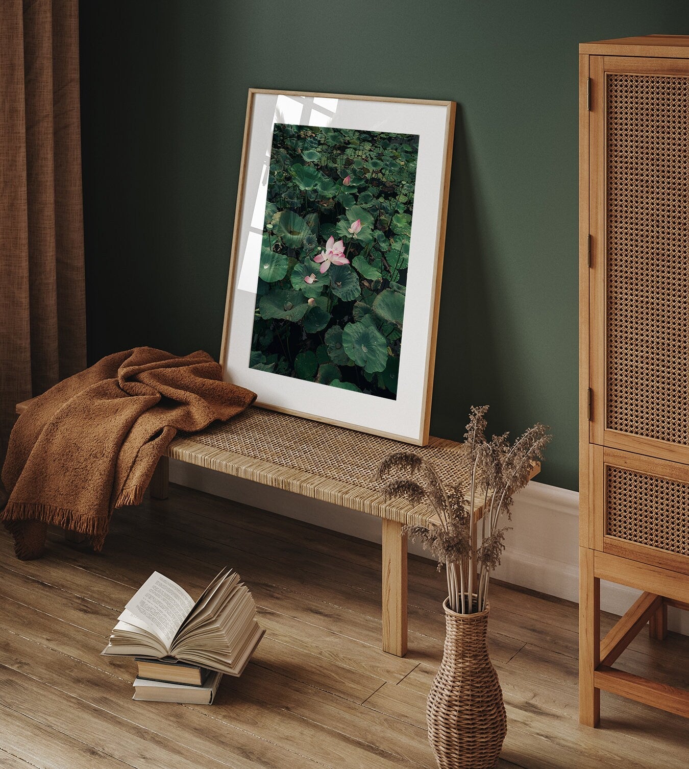 The Lotus framed art decorates a woven bench with a cozy blanket, an open book, and dried flowers in a stylish room.