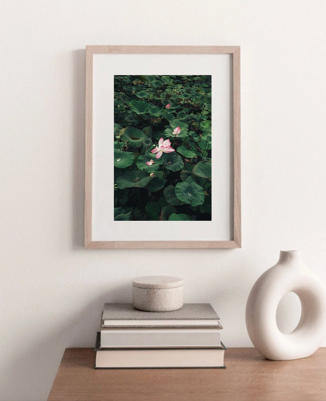Framed Lotus photo next to a round abstract vase, above books on a shelf.
