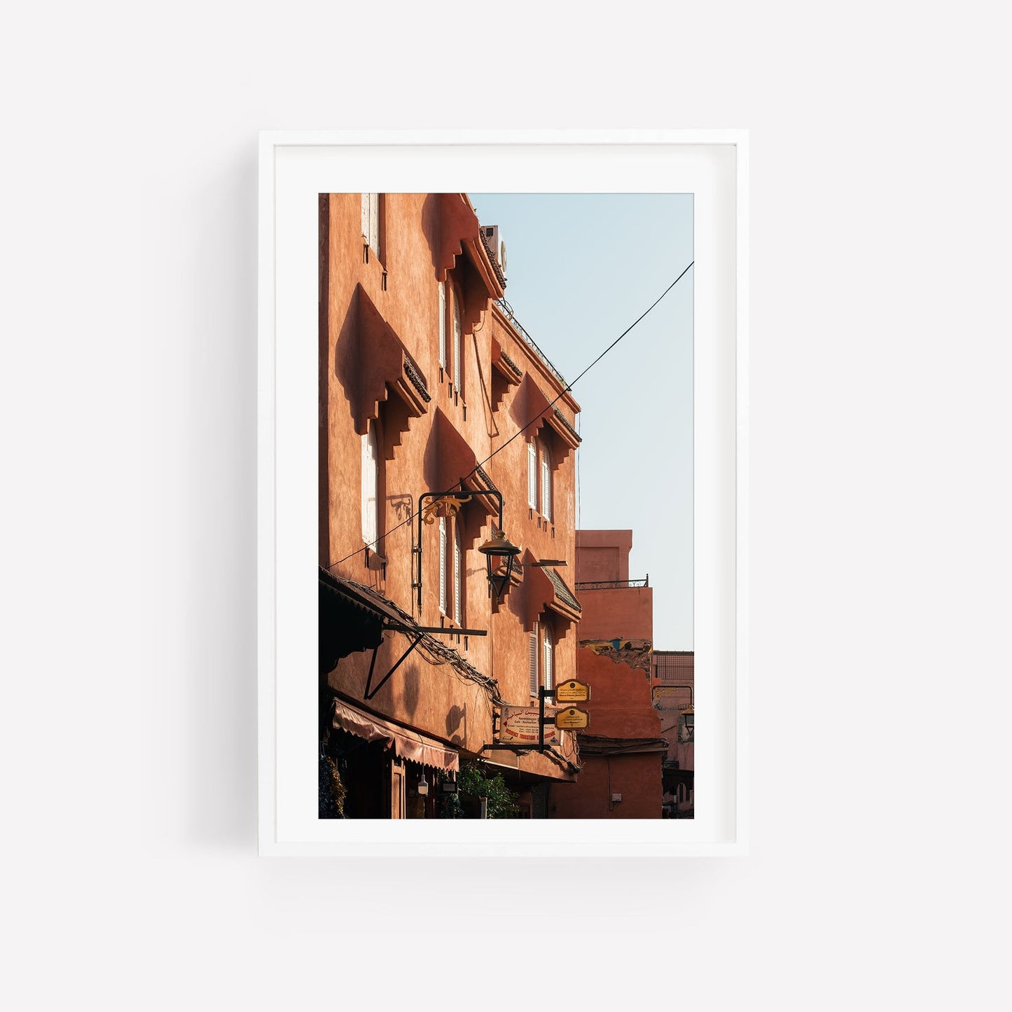 Framed photo of Marrakesh Red Building featuring sunlit terracotta, windows, and balconies under a clear sky.