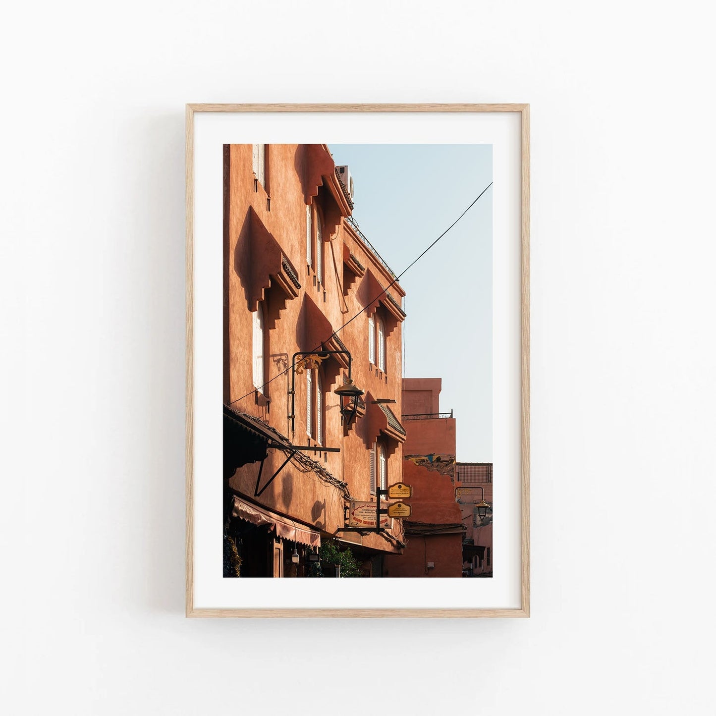 Framed photo titled Marrakesh Red Building depicting orange buildings with windows and wires under a clear blue sky.